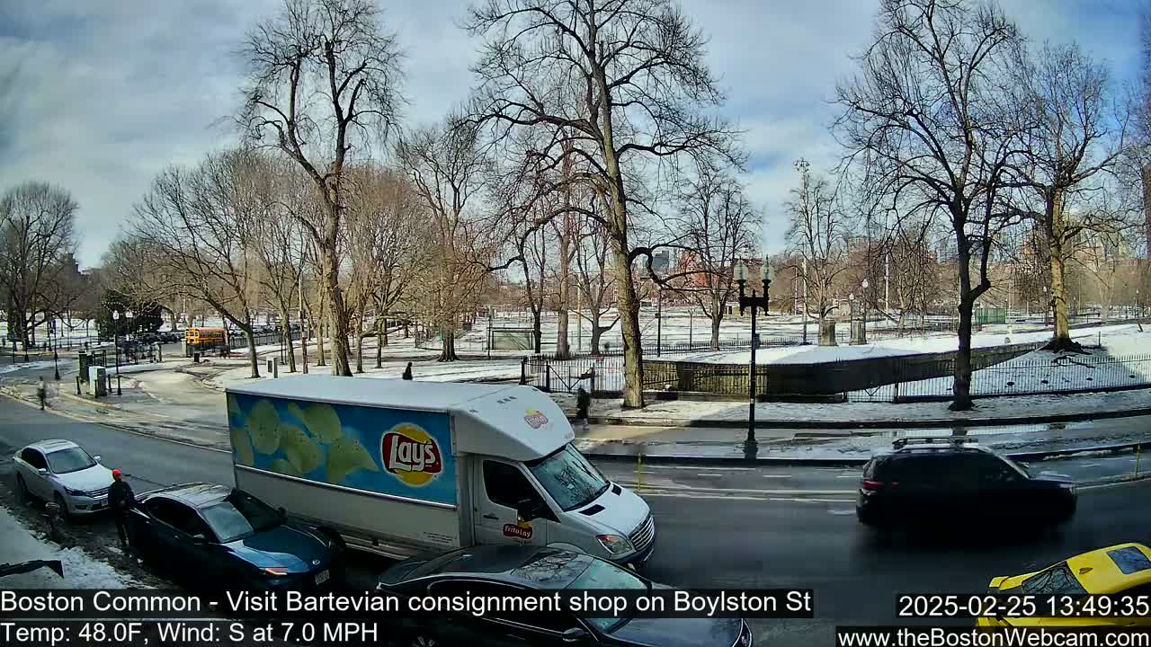 A partly sunny day with snow on the ground and a partly-snow covered park shows a city street with cars and a Lay's chip delivery truck.