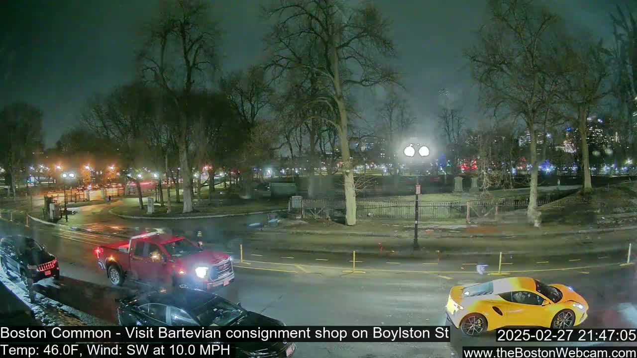A nighttime street scene shows a park with bare trees, wet roads, and several vehicles including a red pickup truck and a yellow sports car under a dark, overcast sky with a southwest wind.