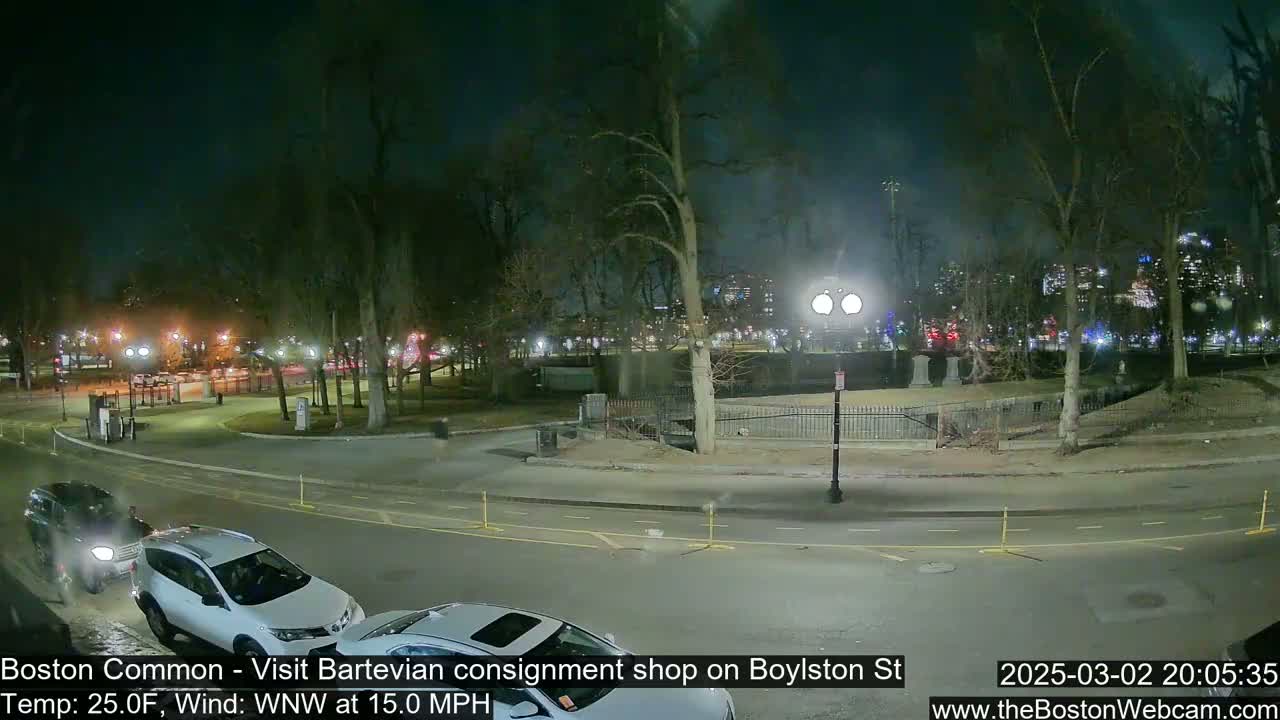 A nighttime view of a park with cars parked along a road, under a dark sky with a 15 mph wind.