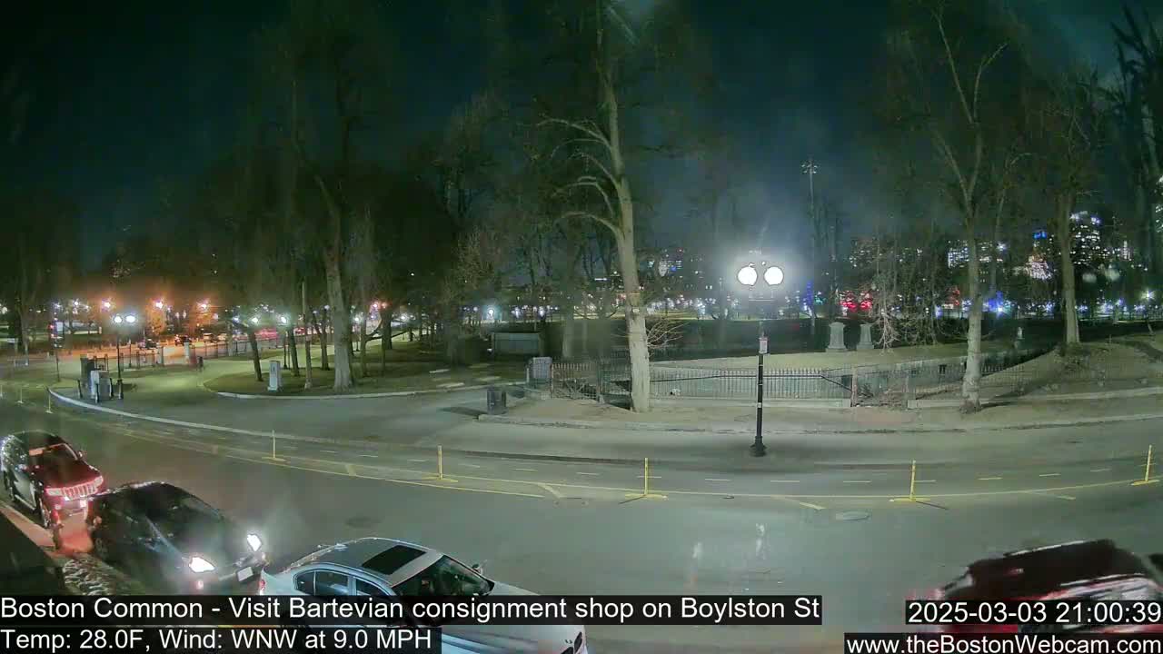 A nighttime view of a park with several cars on a road nearby, under a clear sky with a WNW wind at 9 mph and a temperature of 28°F.