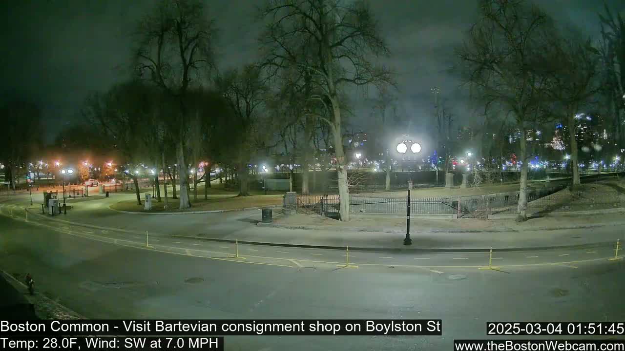 A nighttime view of a park with bare trees, streetlights, and a roadway, under a cloudy sky, with a southwest wind at 7 mph and a temperature of 28 degrees Fahrenheit.