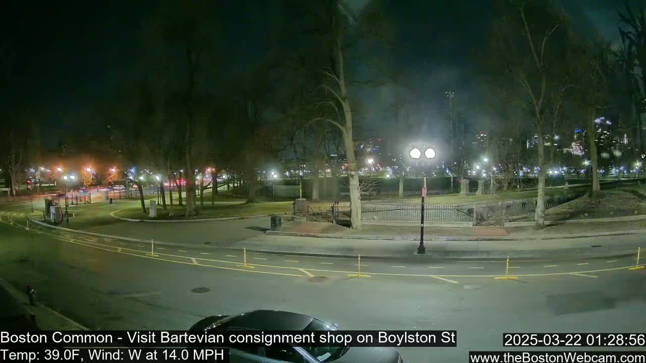 A nighttime view of a park with a road and sparse traffic under a dark sky, with a 39°F temperature and a 14 mph west wind.