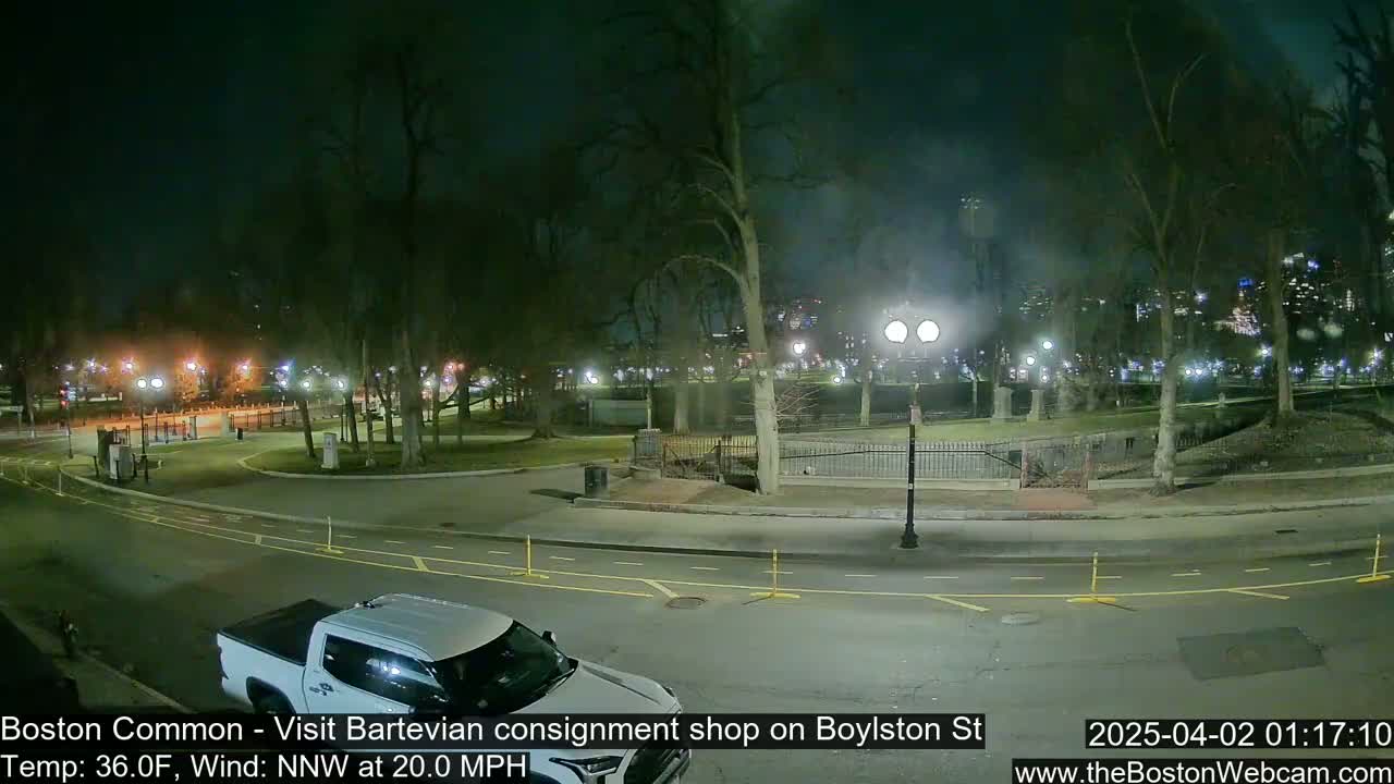 A nighttime view of a park, with a white pickup truck parked near a street, under a windy, 36°F night.