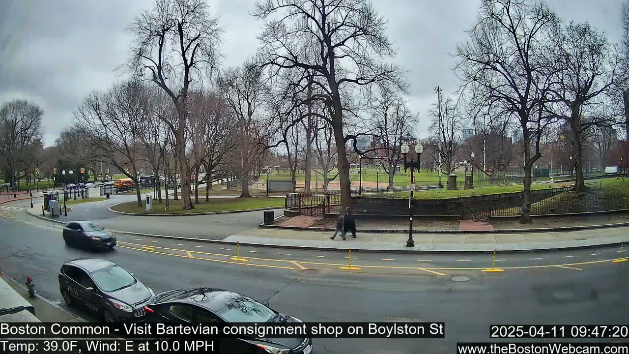 A partly cloudy day shows bare trees surrounding a park with a road and several cars visible.