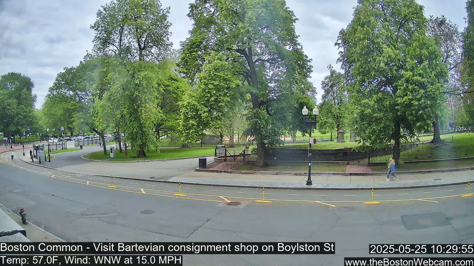 A partly cloudy day with a WNW wind at 15 mph shows a street scene alongside a park with green trees and grass, featuring a person walking.