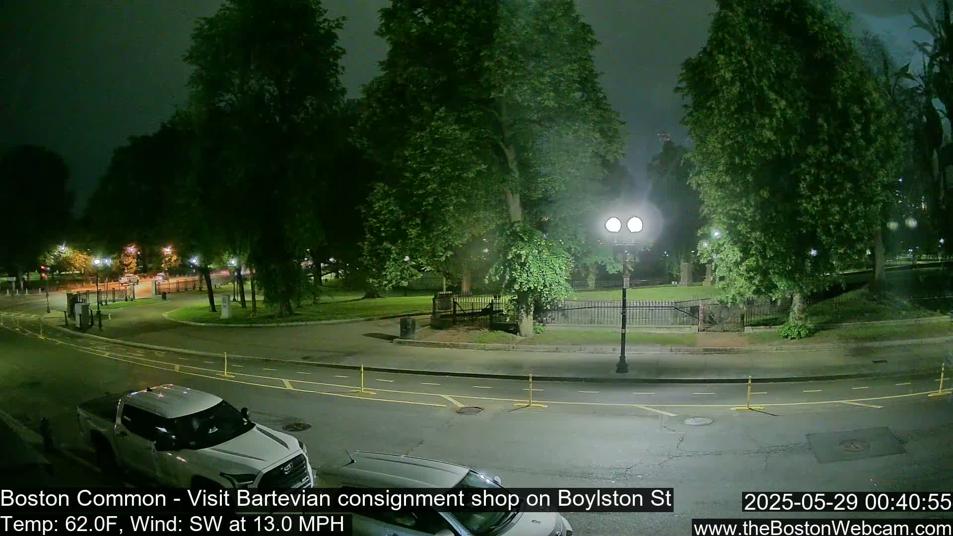 A nighttime view of a park with a street and parked vehicles, under a partly cloudy sky with a southwest wind.