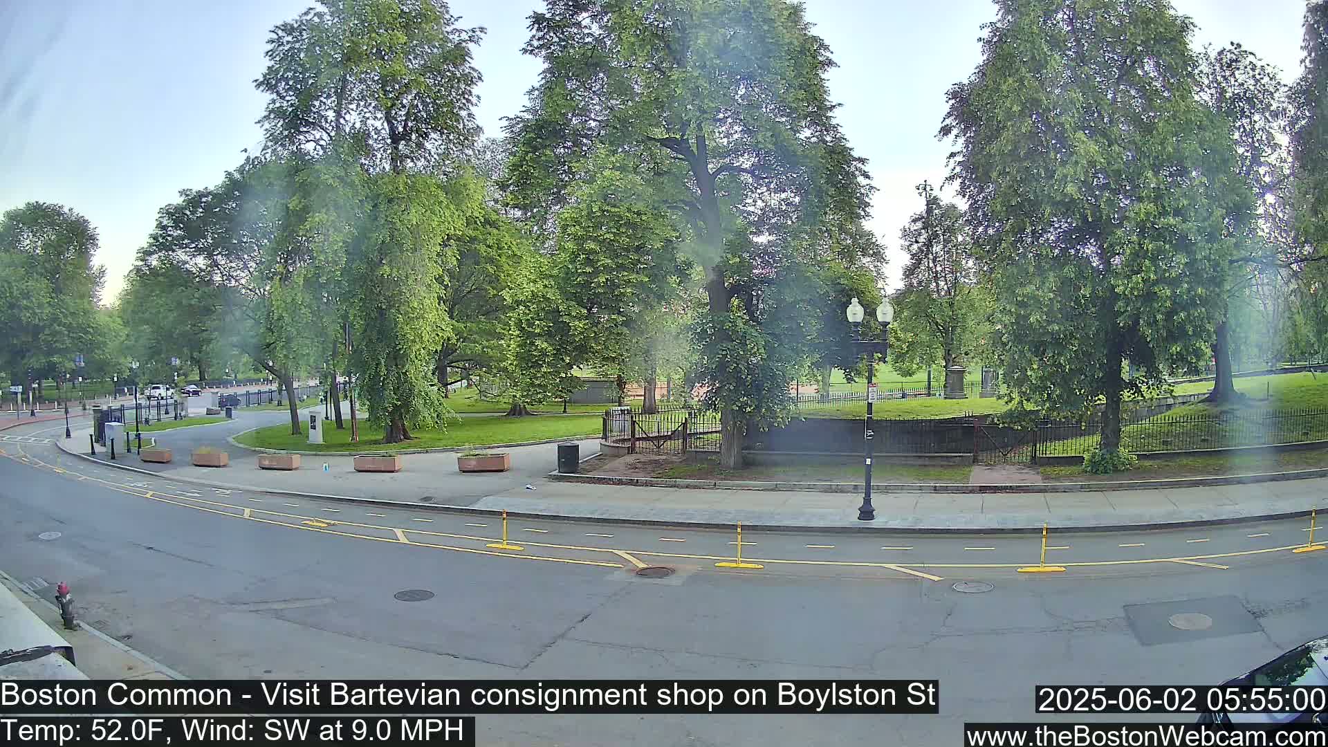 A partly sunny view of a park with lush green trees and a curving road, under a light southwest wind.
