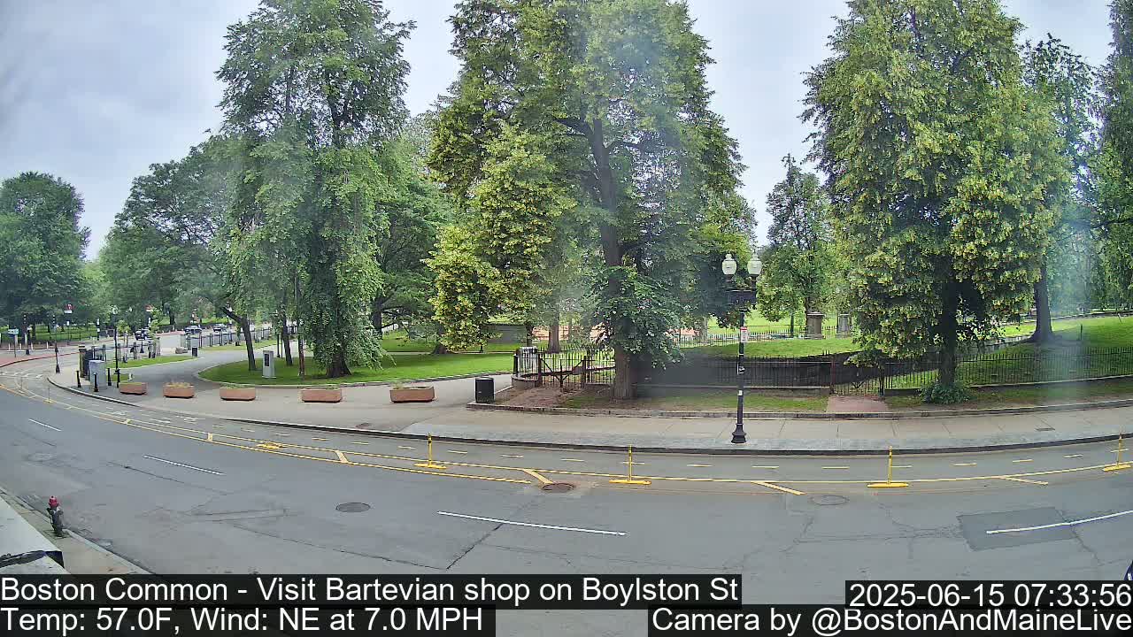 A partly cloudy day shows a street curving past a park with lush green trees and a paved walkway.