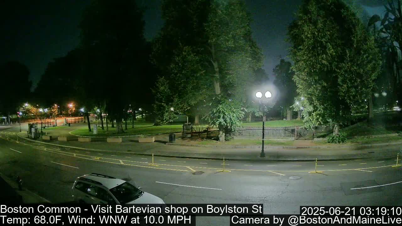 A nighttime street scene shows a park with trees and a lamppost, a roadway with a vehicle, and a calm wind.