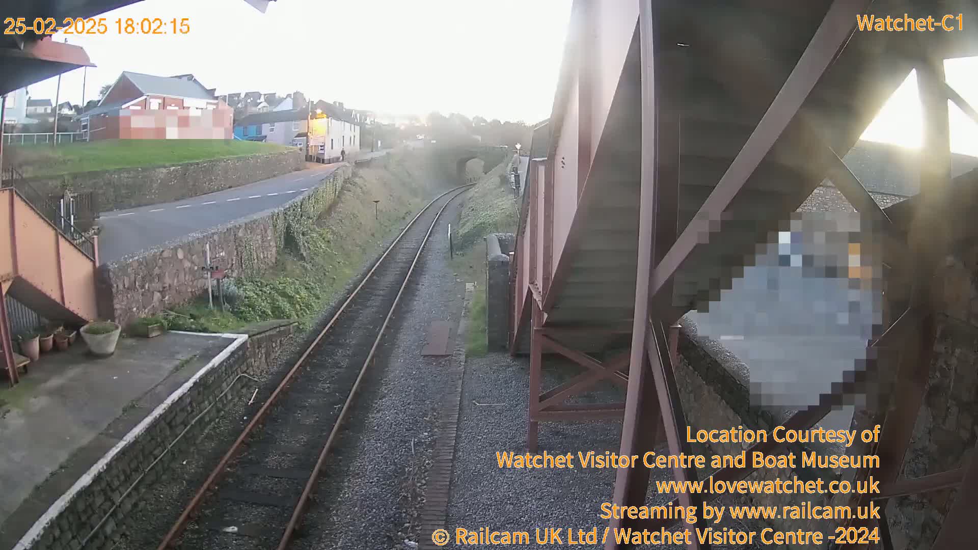 A view from a footbridge shows train tracks, a road, and buildings on a hazy day.