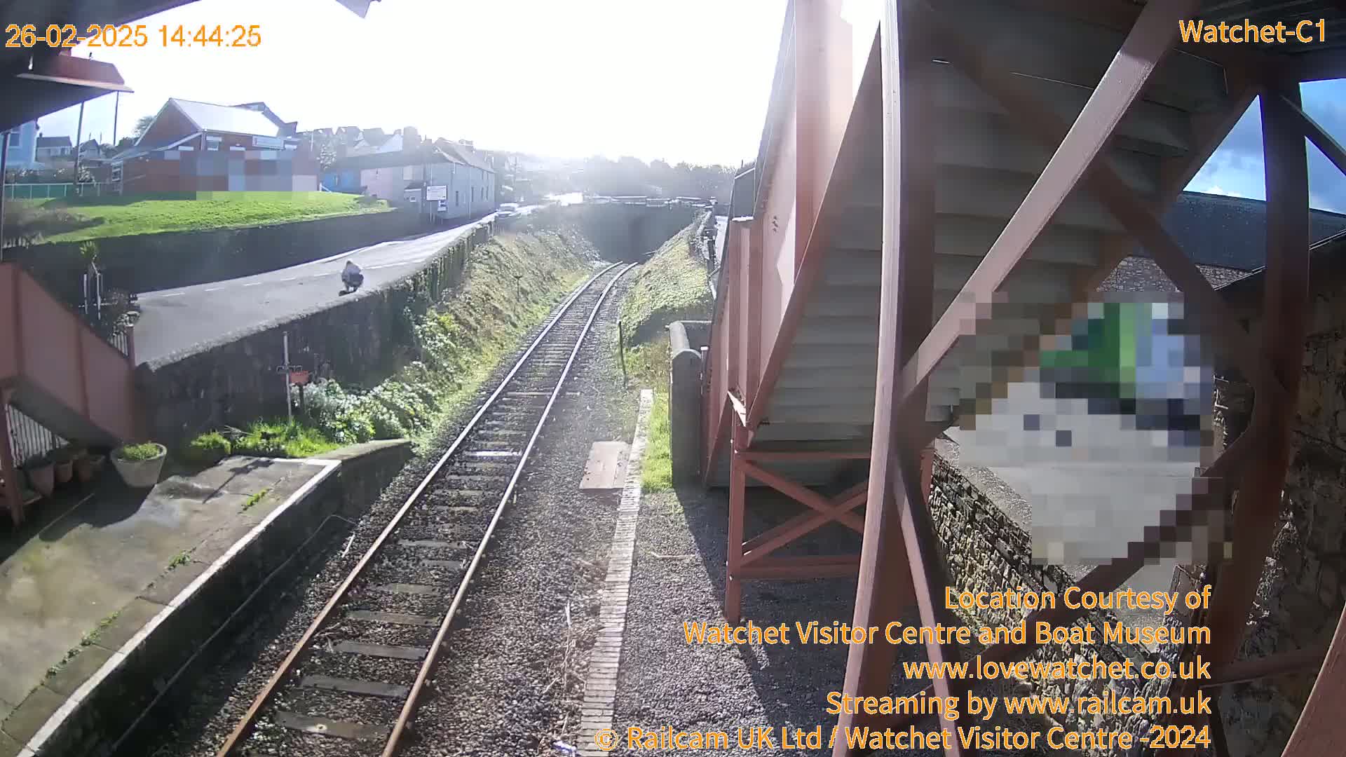 A sunny view of a train track alongside a road and a small town, with a person visible on the road.