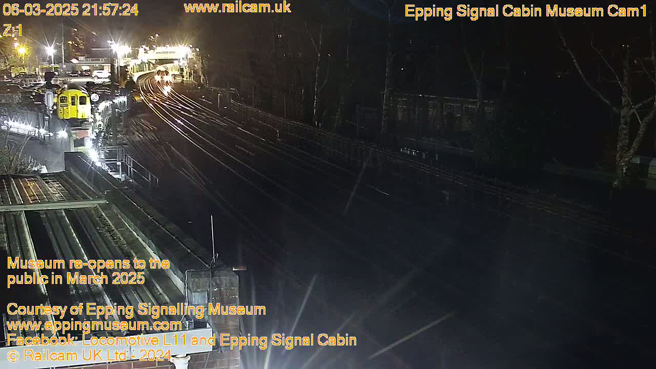 A nighttime view of a train station with a yellow train visible and multiple train tracks extending into the darkness.