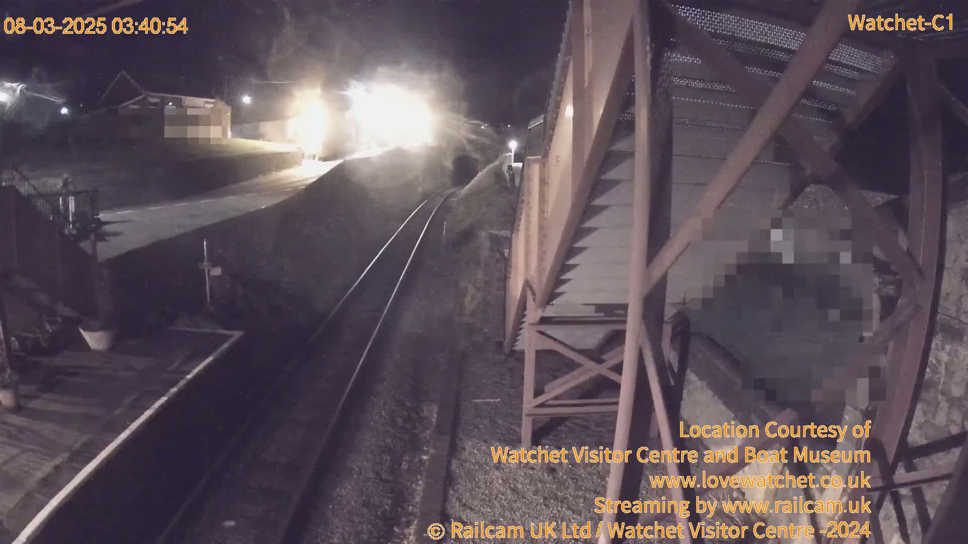A nighttime view of a train passing by a railway station, with lights illuminating the scene.