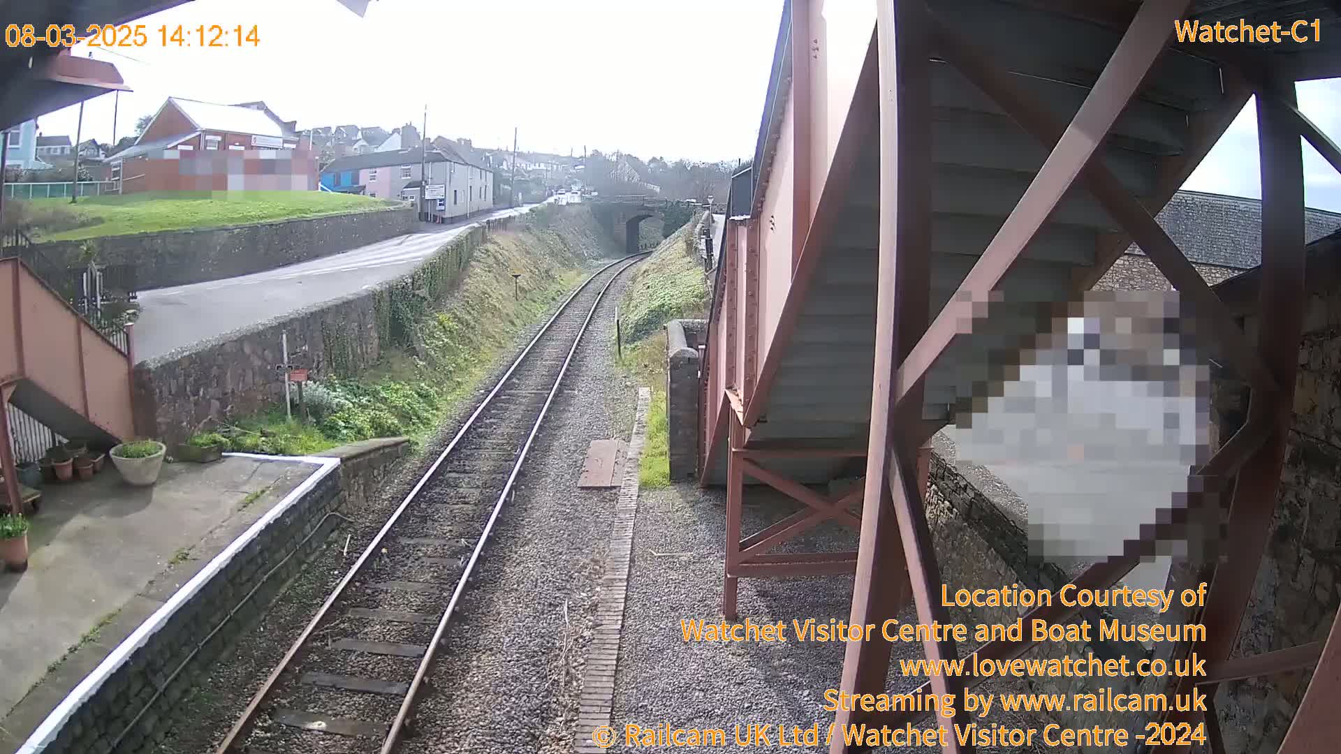 A high-angle view of a railway track and a roadway next to a stone wall on an overcast day.