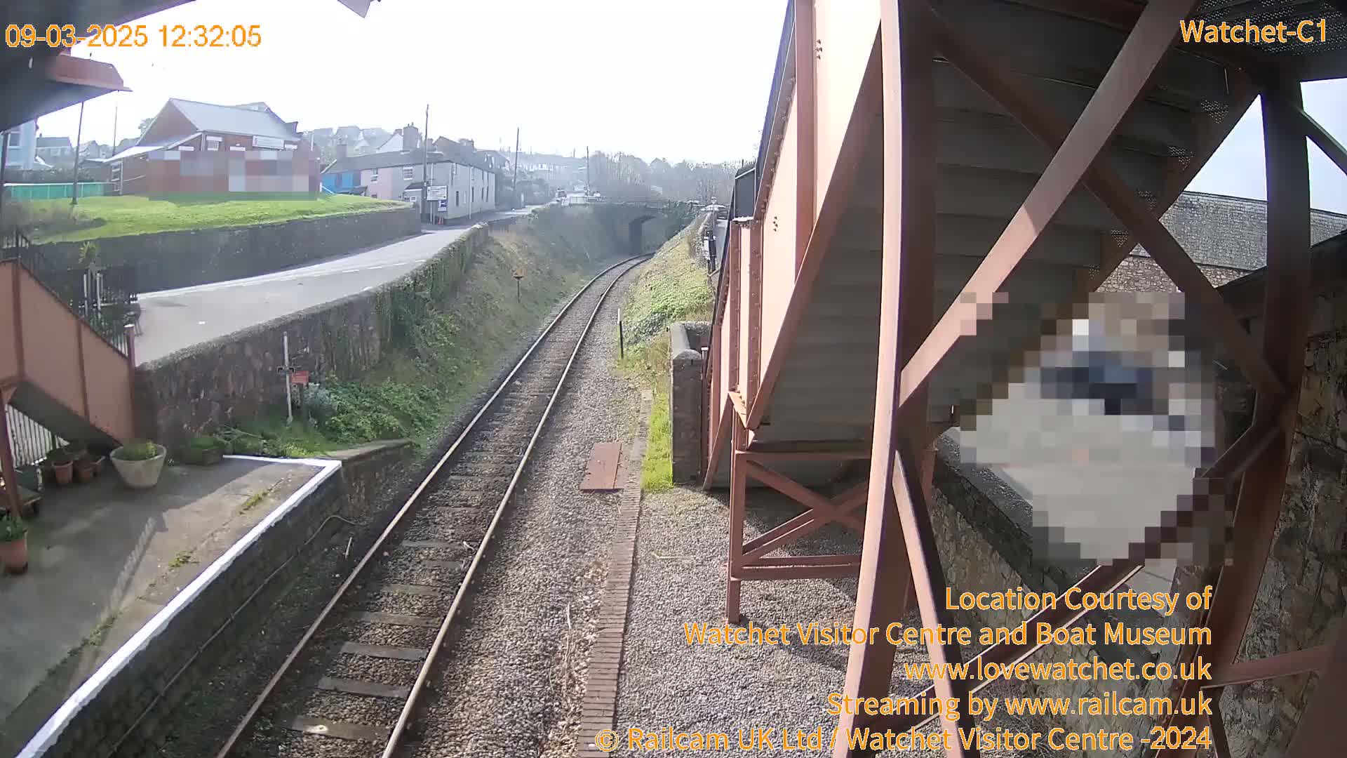 A sunny view of train tracks and a small town from a metal footbridge.