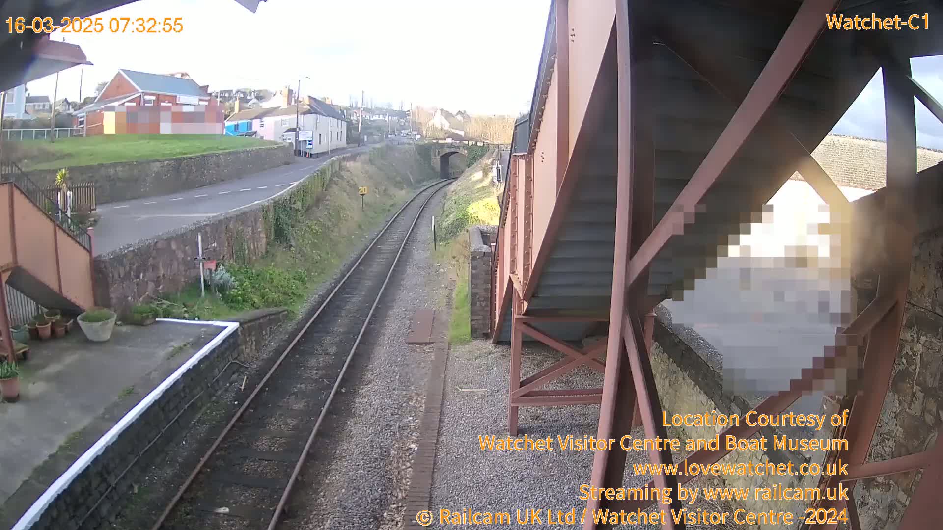 A view from a footbridge overlooking a train track on a sunny day, with a small town visible in the distance.