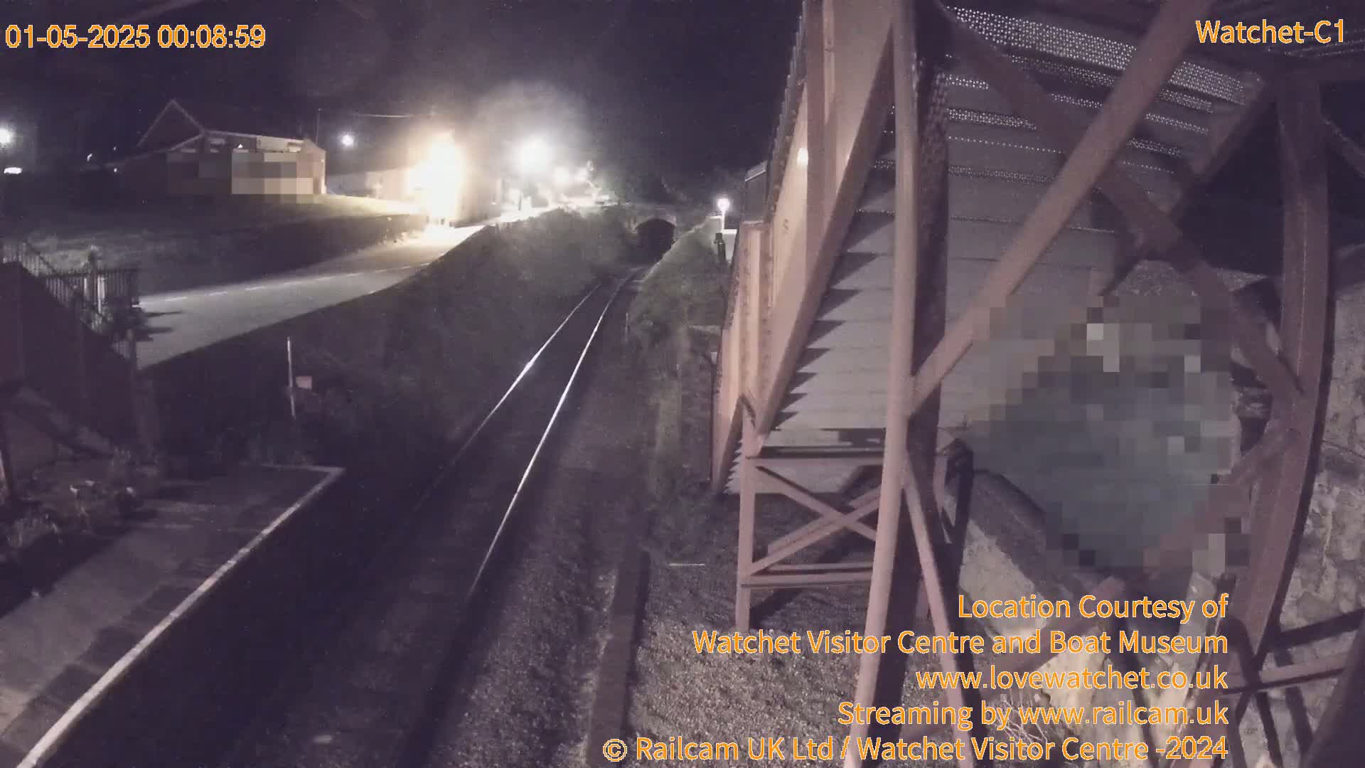 A nighttime view of train tracks and a railway platform, with a building visible in the distance under artificial light.