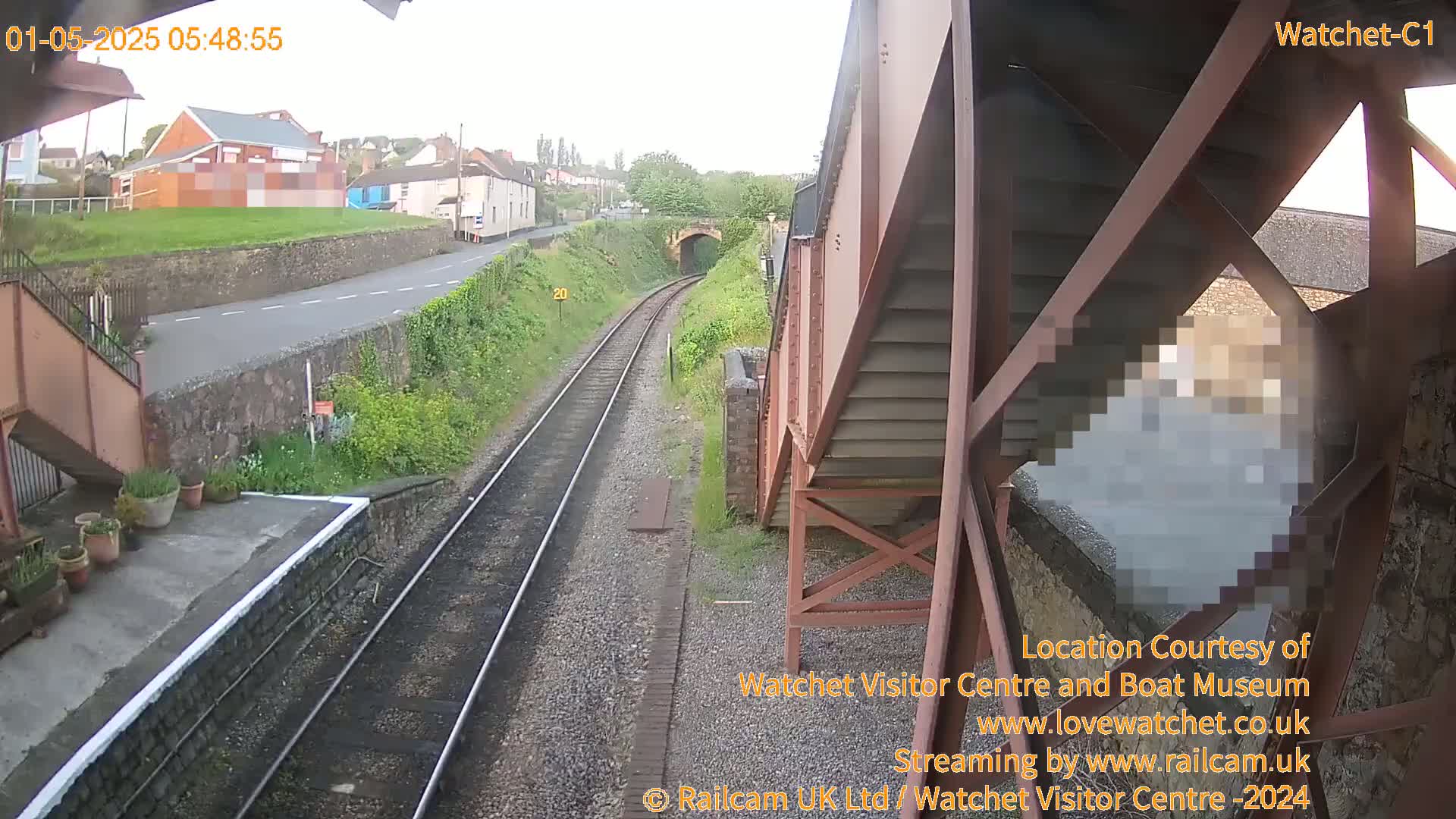 A view from a railway bridge on an overcast day shows train tracks leading to a tunnel under a road and some buildings in the distance.