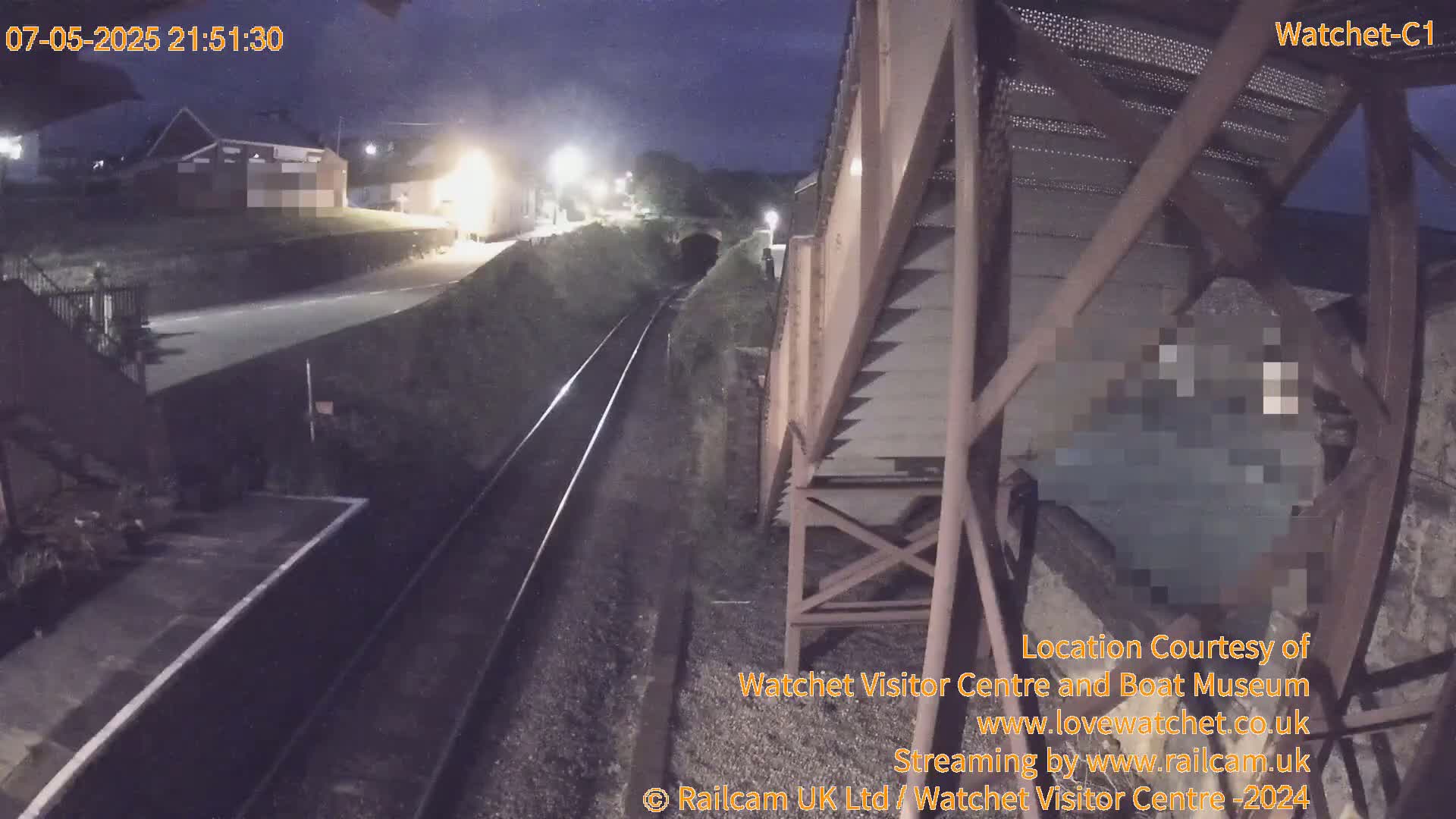 A nighttime view of a railway track and a nearby building, seen from a high vantage point on a structure.