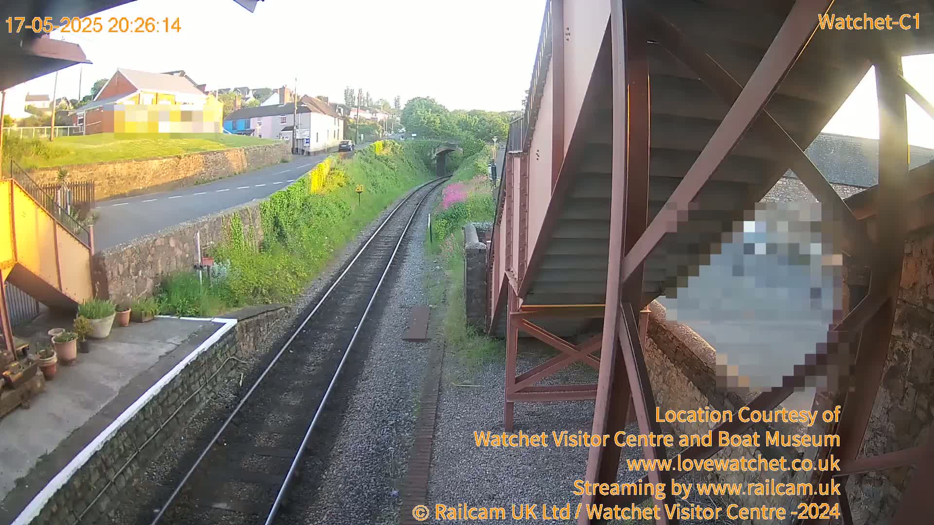 A view from a railway footbridge at dusk shows railway tracks extending into a tunnel, passing alongside a road and residential buildings.