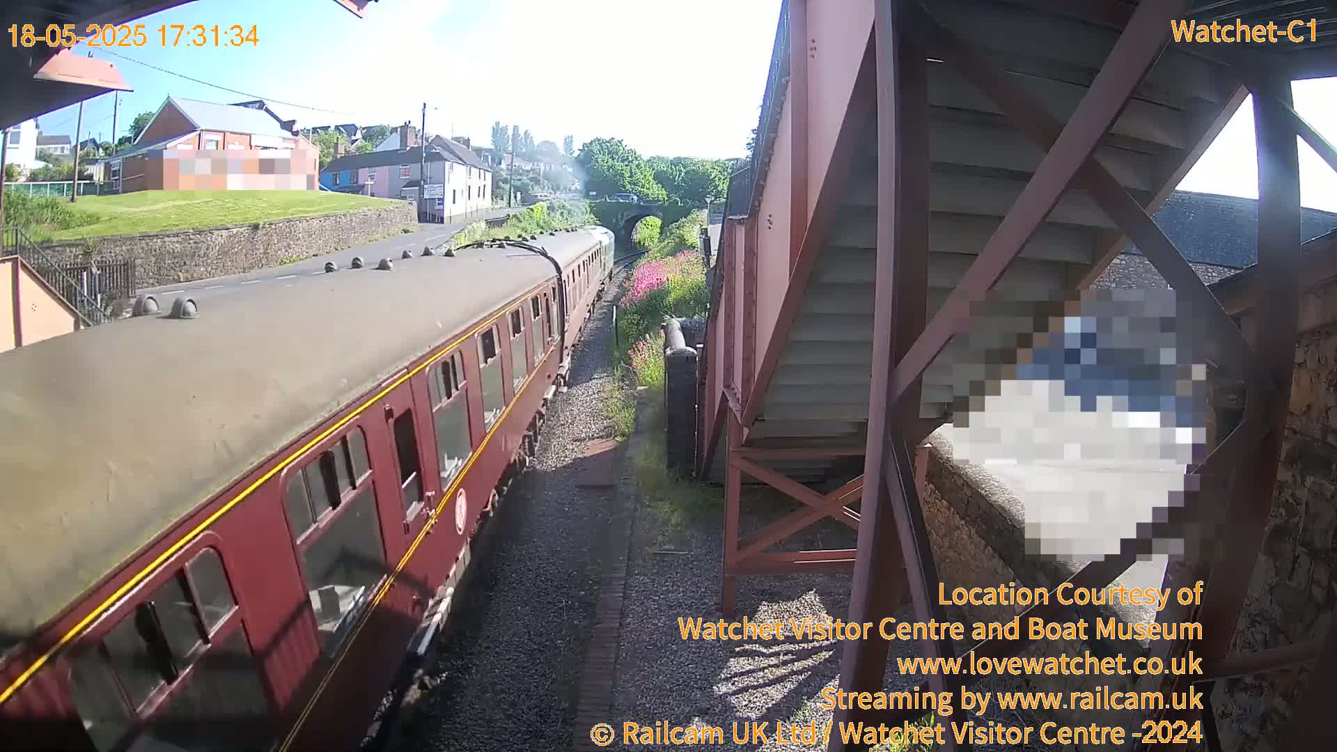 A maroon passenger train is seen passing by a railway bridge on a sunny day.