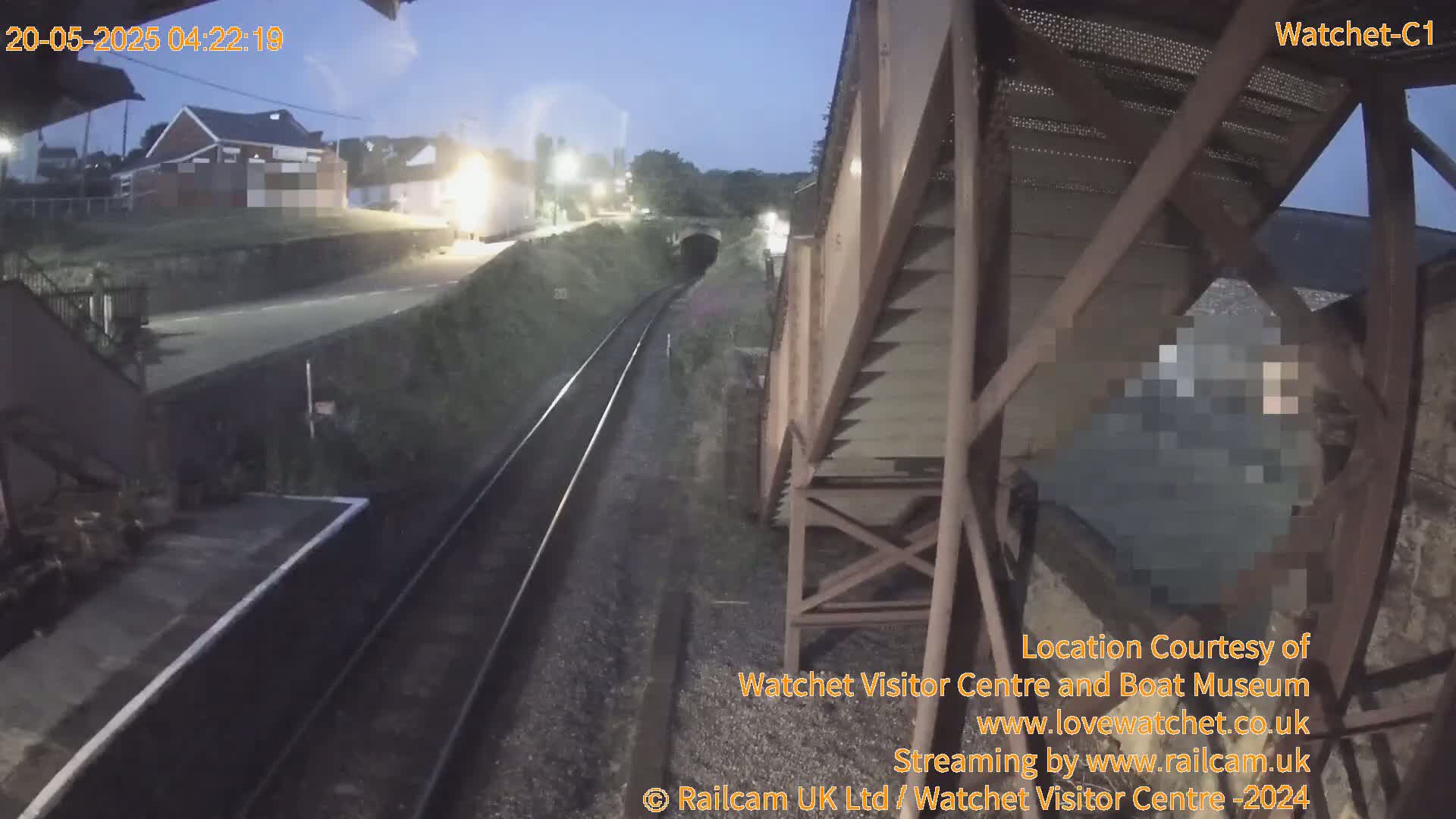 A nighttime view of a railway track leading to a tunnel, with a person obscured under a railway bridge in the foreground.