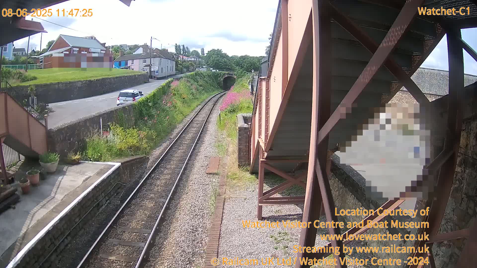 A train track runs alongside a road, passing a small town under a partly cloudy sky.