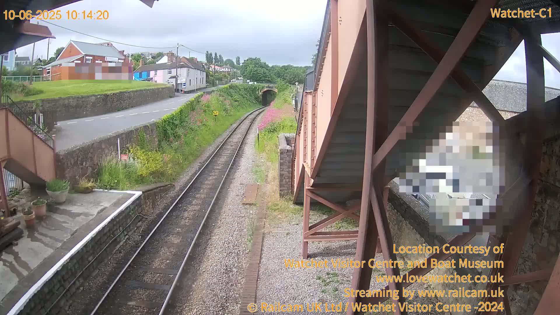 A view from a railway bridge on an overcast day shows train tracks leading to a tunnel, with a road and buildings in the background.