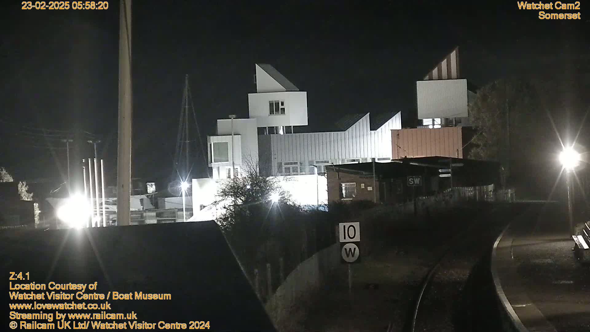A modern, multi-level white building complex is illuminated at night, adjacent to railroad tracks under dark skies.