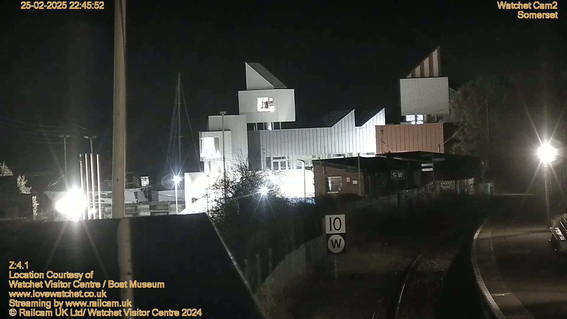 A modern, multi-sectioned building is illuminated at night, adjacent to railway tracks.