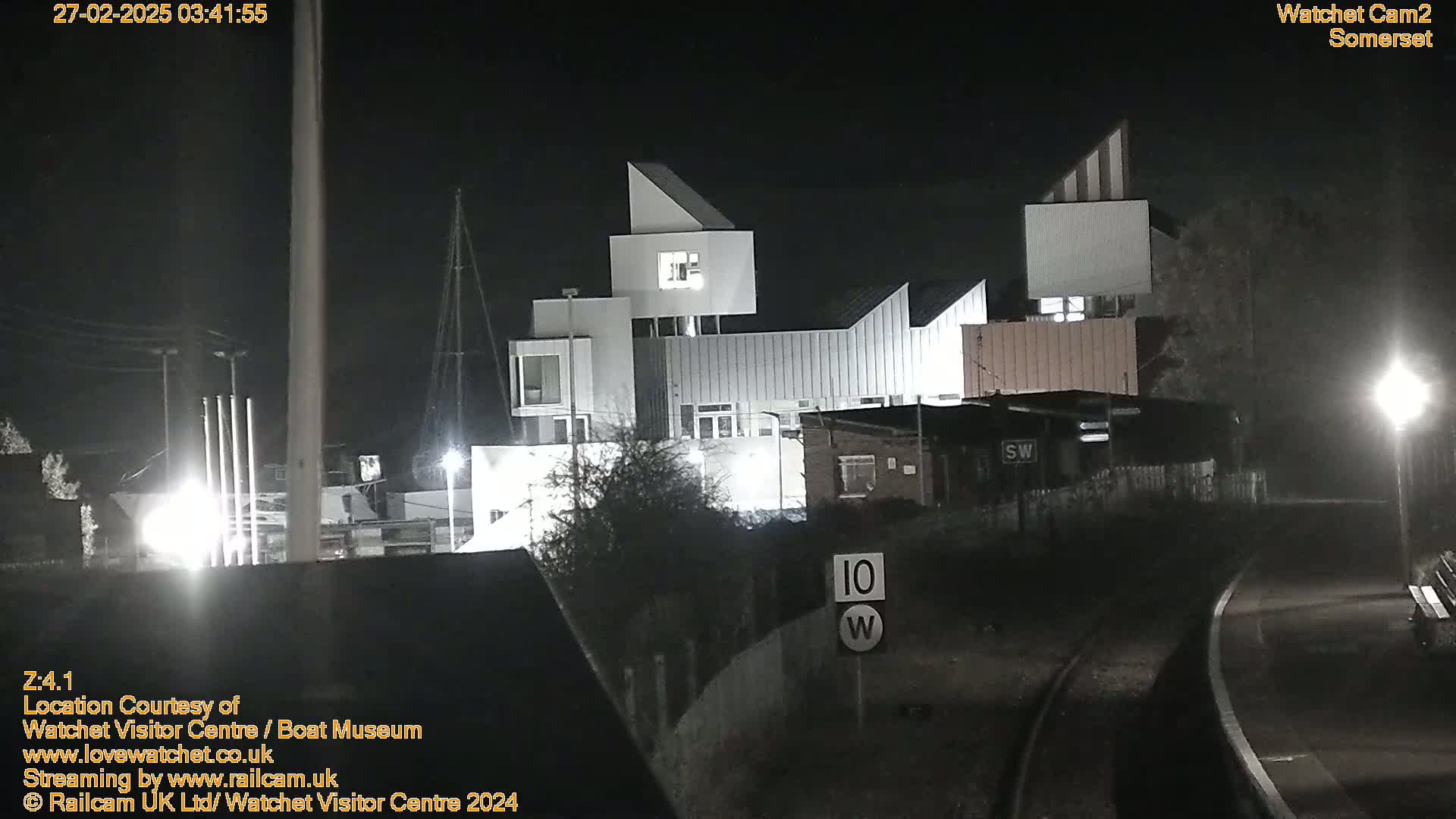 A modern, white building is illuminated at night near a railway track and a street light.