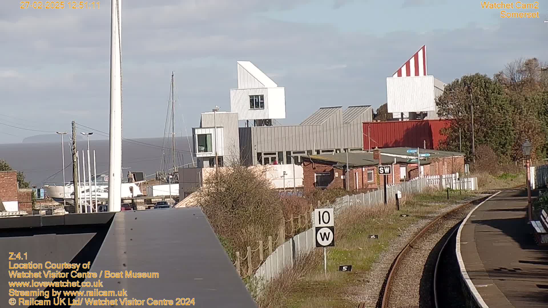 A view of a harbor with boats, modern buildings, and a railway track on a sunny day.