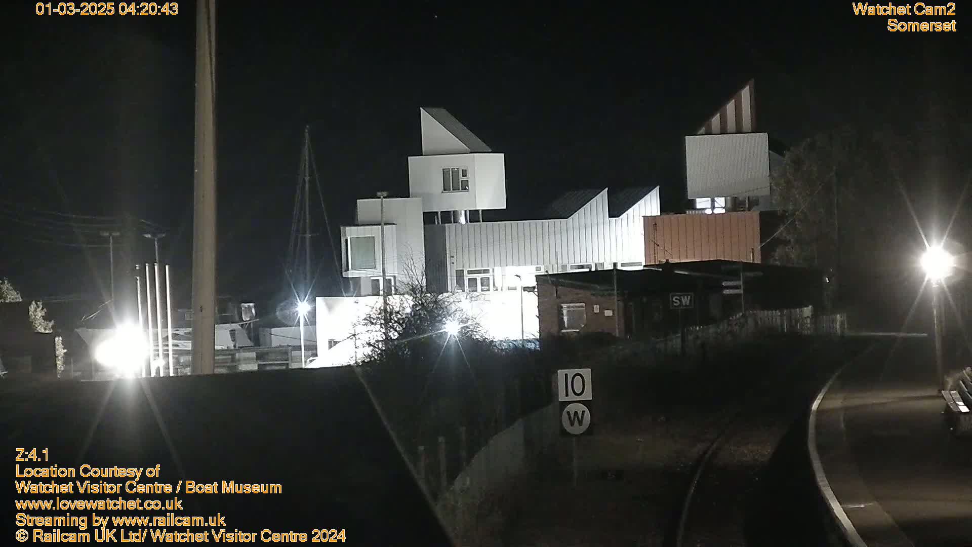 A modern, multi-level building is illuminated at night, next to a railway line.