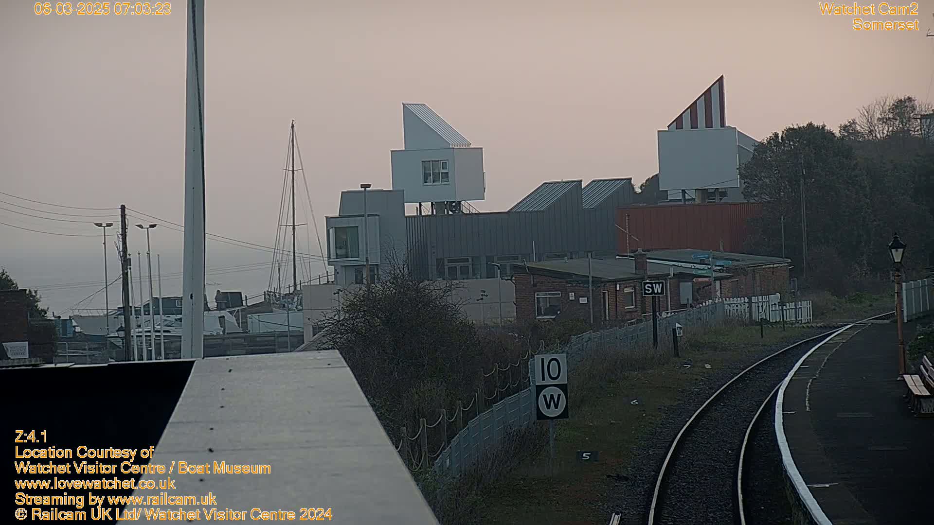A view of a harbor with boats, modern buildings, and train tracks under an overcast sky.