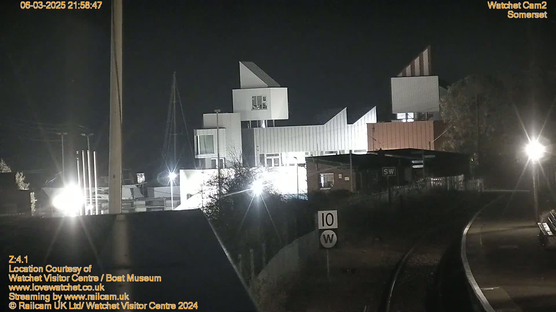 At night, a modern, multi-level building is brightly lit near railroad tracks.