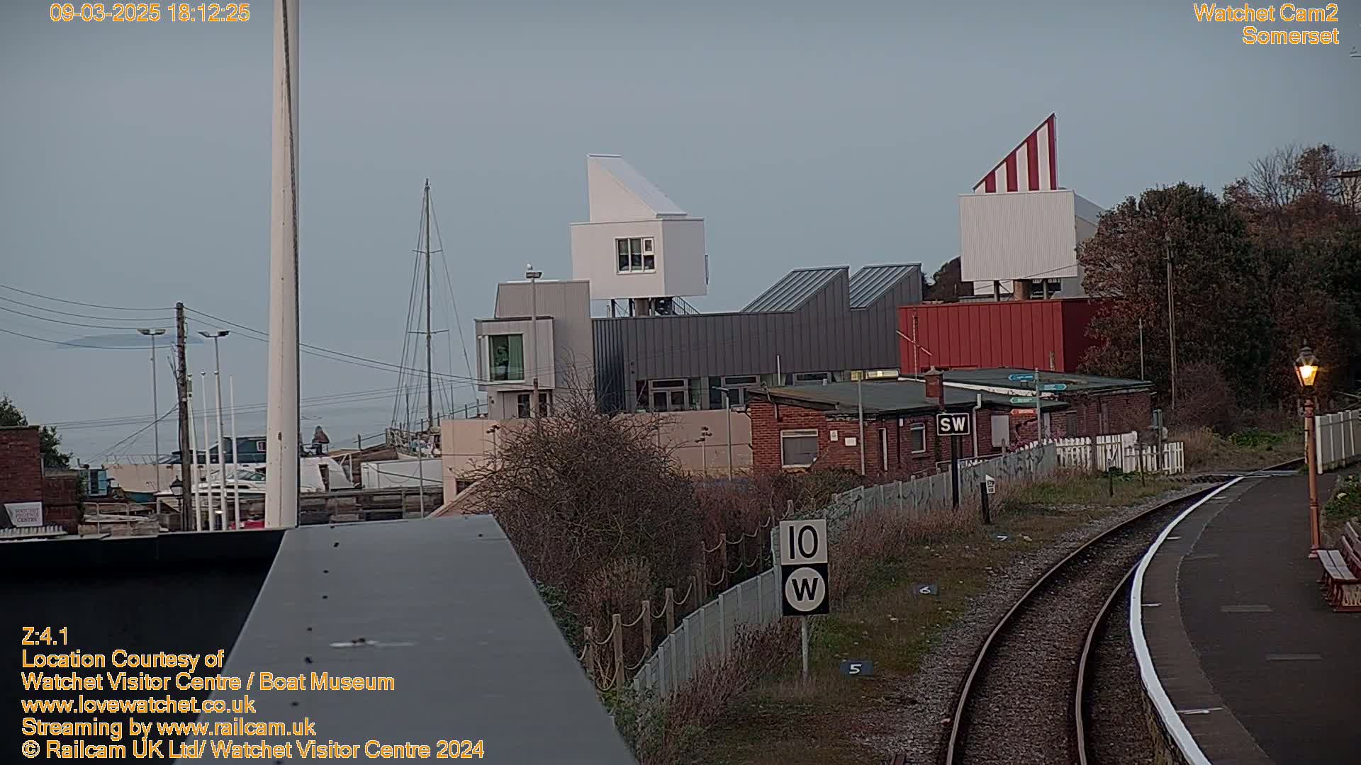 A view of a harbor with modern buildings, a train track, and overcast skies.