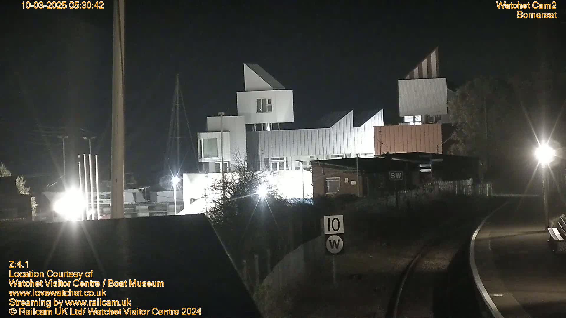 A modern, multi-story white building is illuminated at night near railroad tracks.