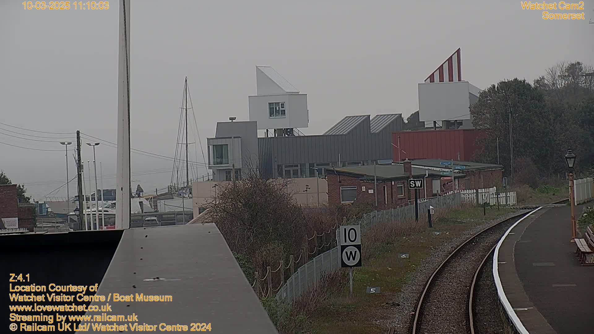 A view of a harbor with modern buildings, a train track, and overcast skies.