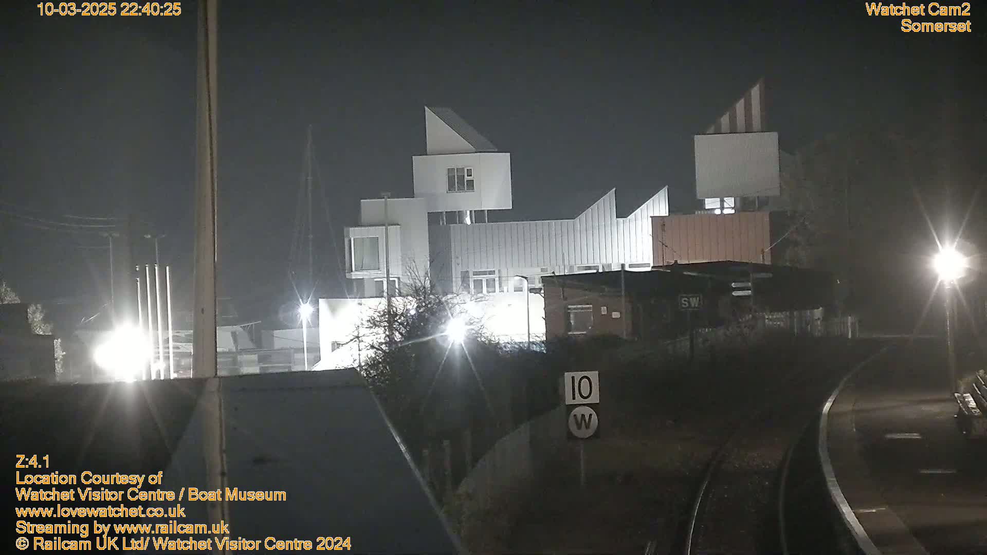 A nighttime, foggy view of a modern, multi-story building complex near a railway track.
