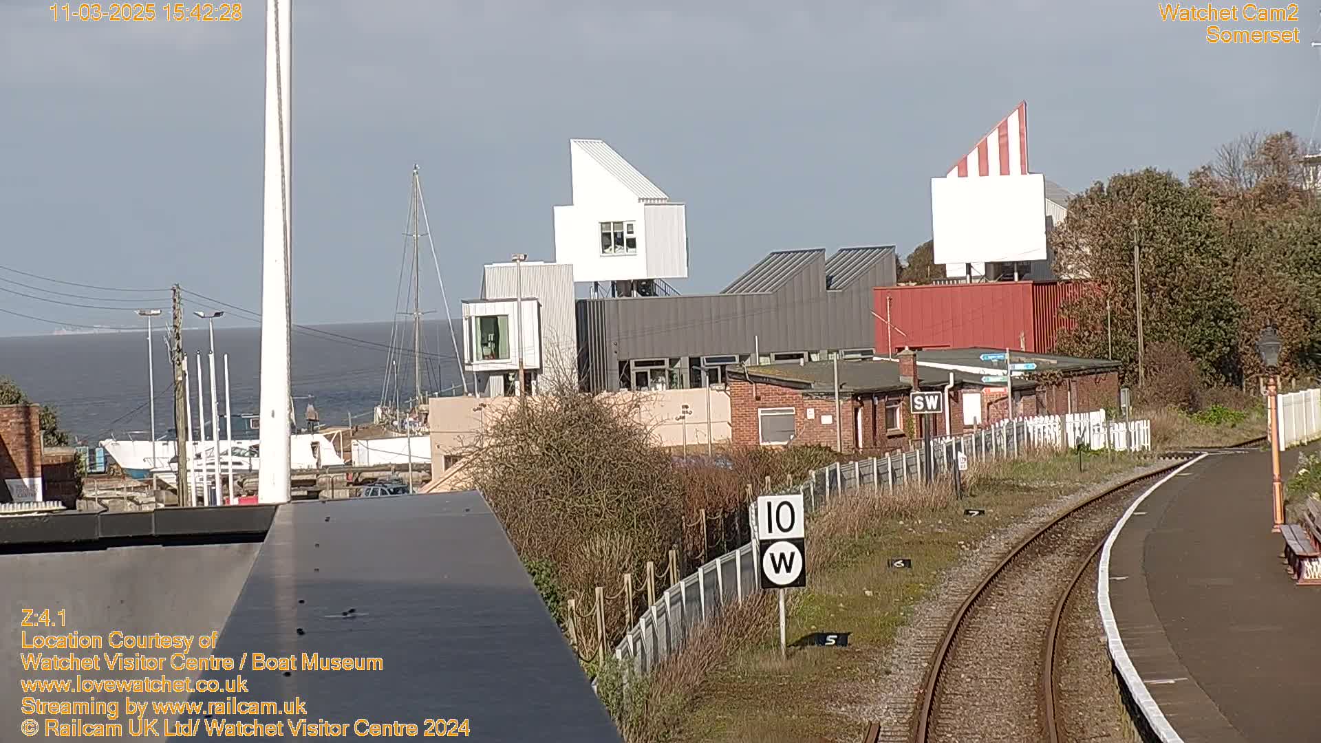 A view of a harbor with modern buildings and a train track under a sunny sky.