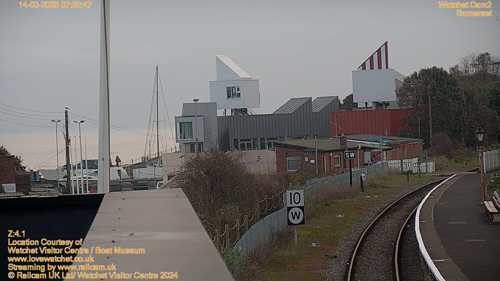 A modern building complex near a harbor and train tracks under an overcast sky.