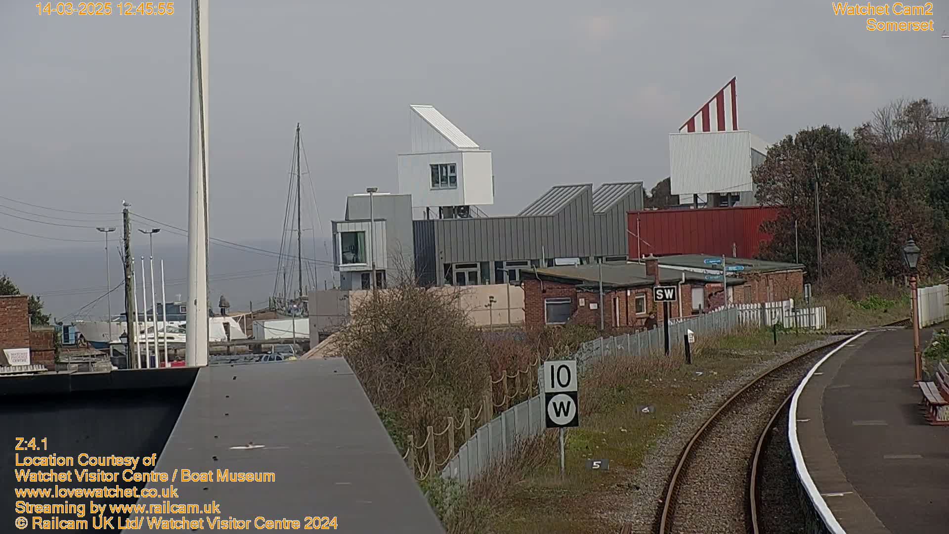 A view of a harbor with modern buildings and a railway track on a slightly hazy day.