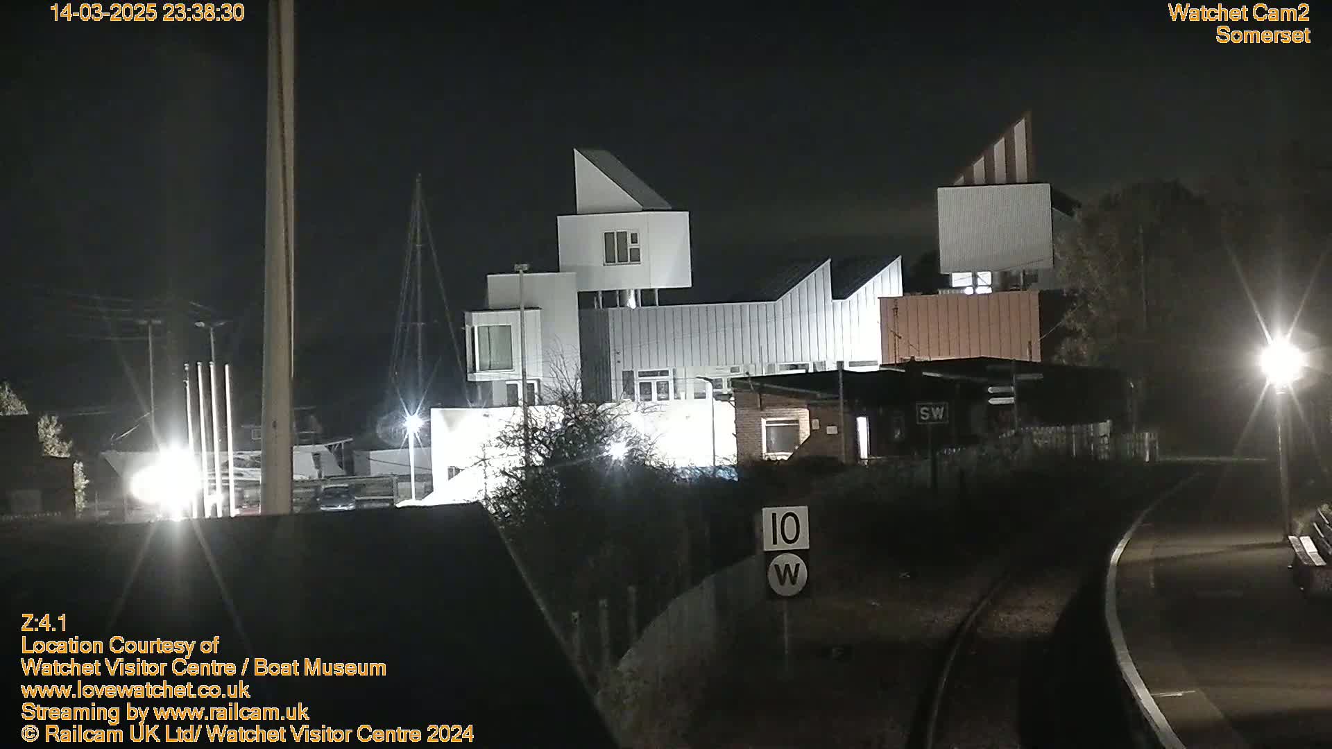 At night, a modern, multi-level white building is illuminated near railroad tracks.