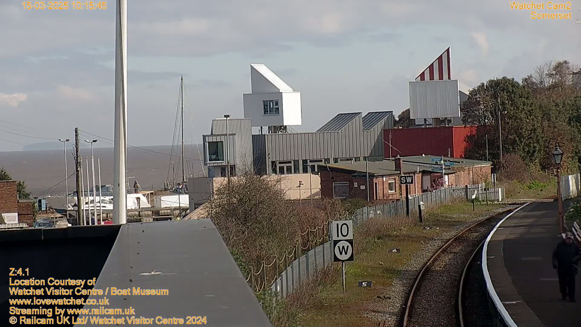 A view of a modern waterfront building complex near a train track on a partly sunny day.