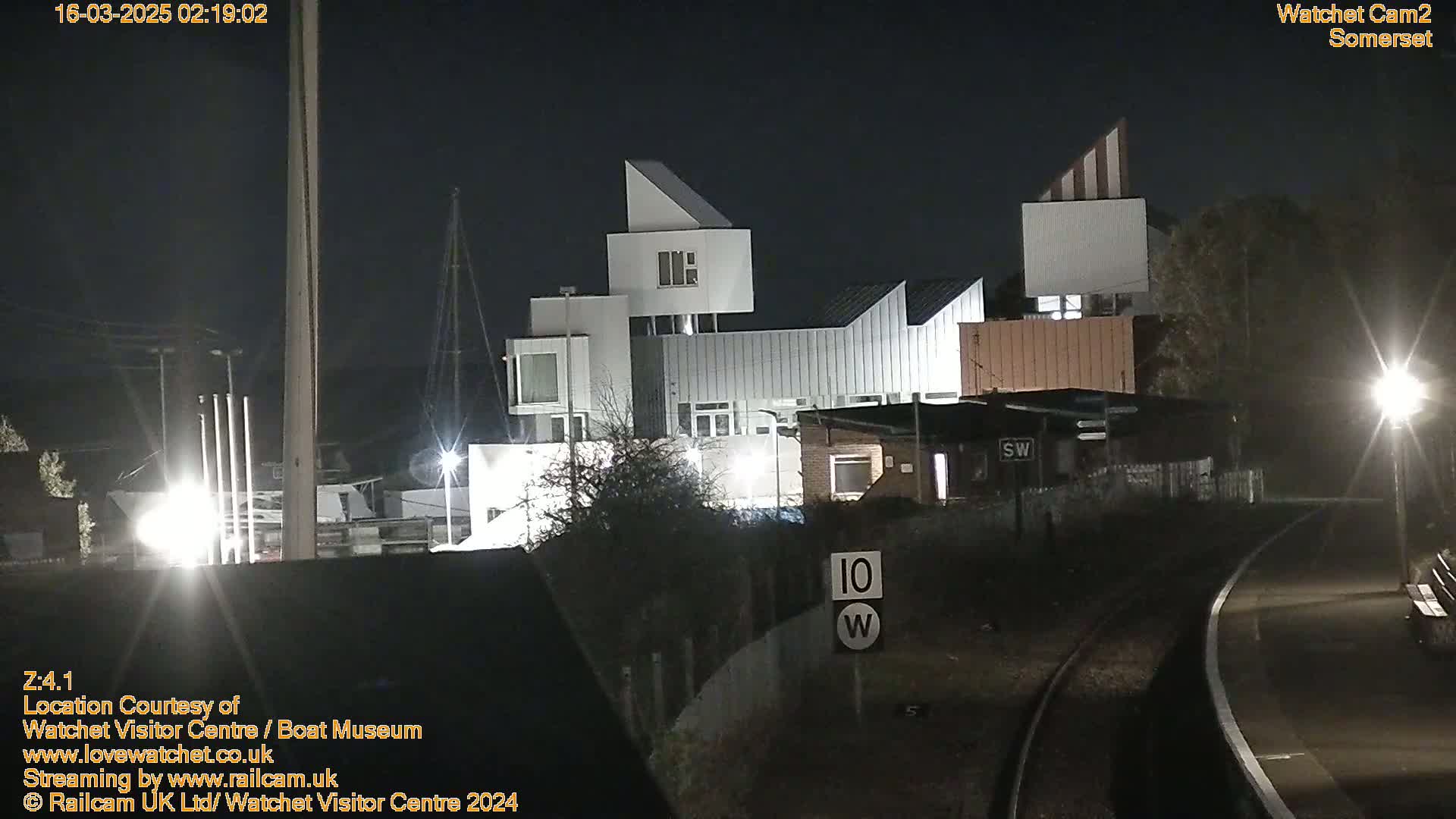 A modern, multi-level building complex is illuminated at night near railroad tracks under a dark sky.