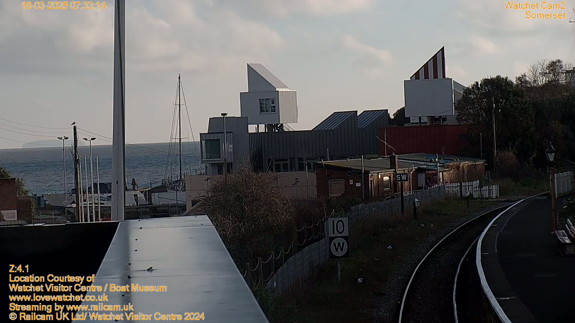 A seaside town viewed from a train, featuring modern architecture near a harbor, under a partly cloudy sky.