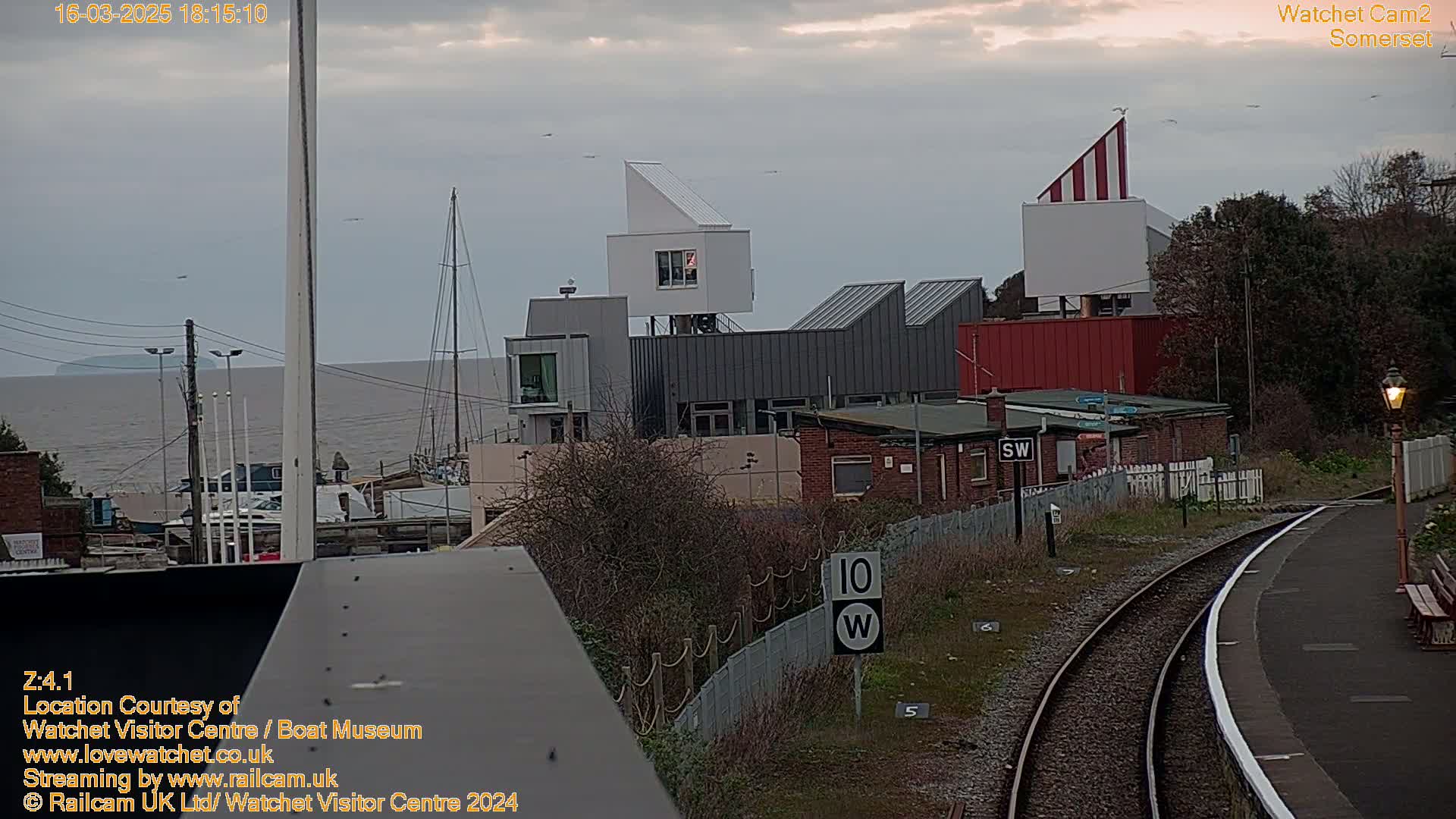 A view from a train overlooking a harbor with modern buildings, a railway track, and an overcast sky.