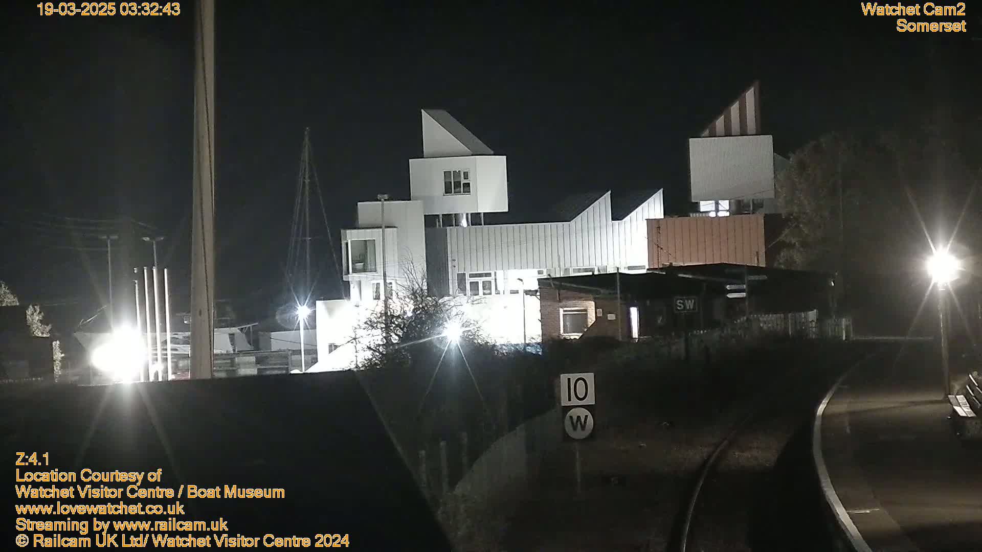 At night, a modern white building complex is illuminated near a railroad track.