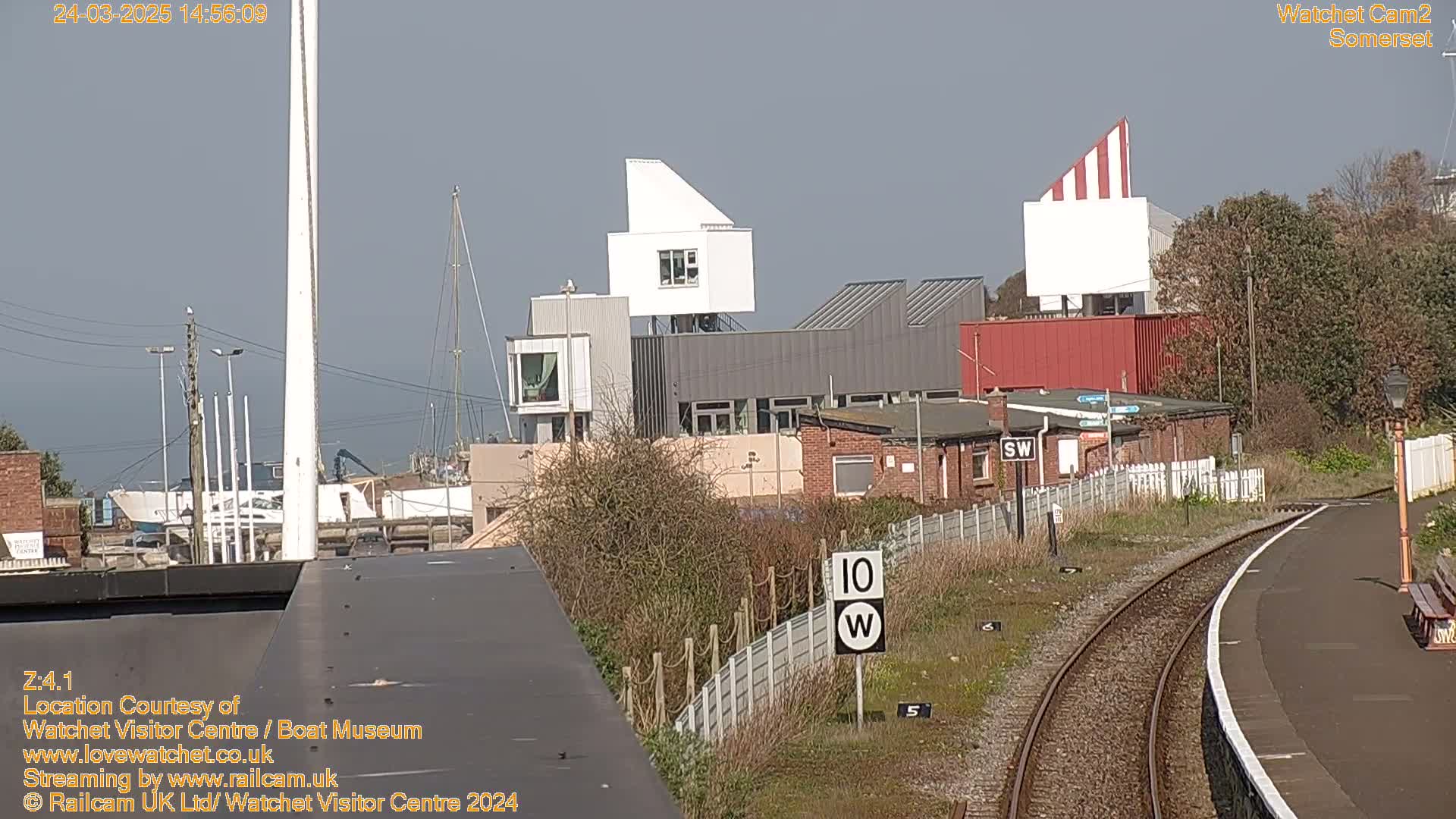A view of a harbor with modern buildings, a railway track, and a mostly sunny sky.