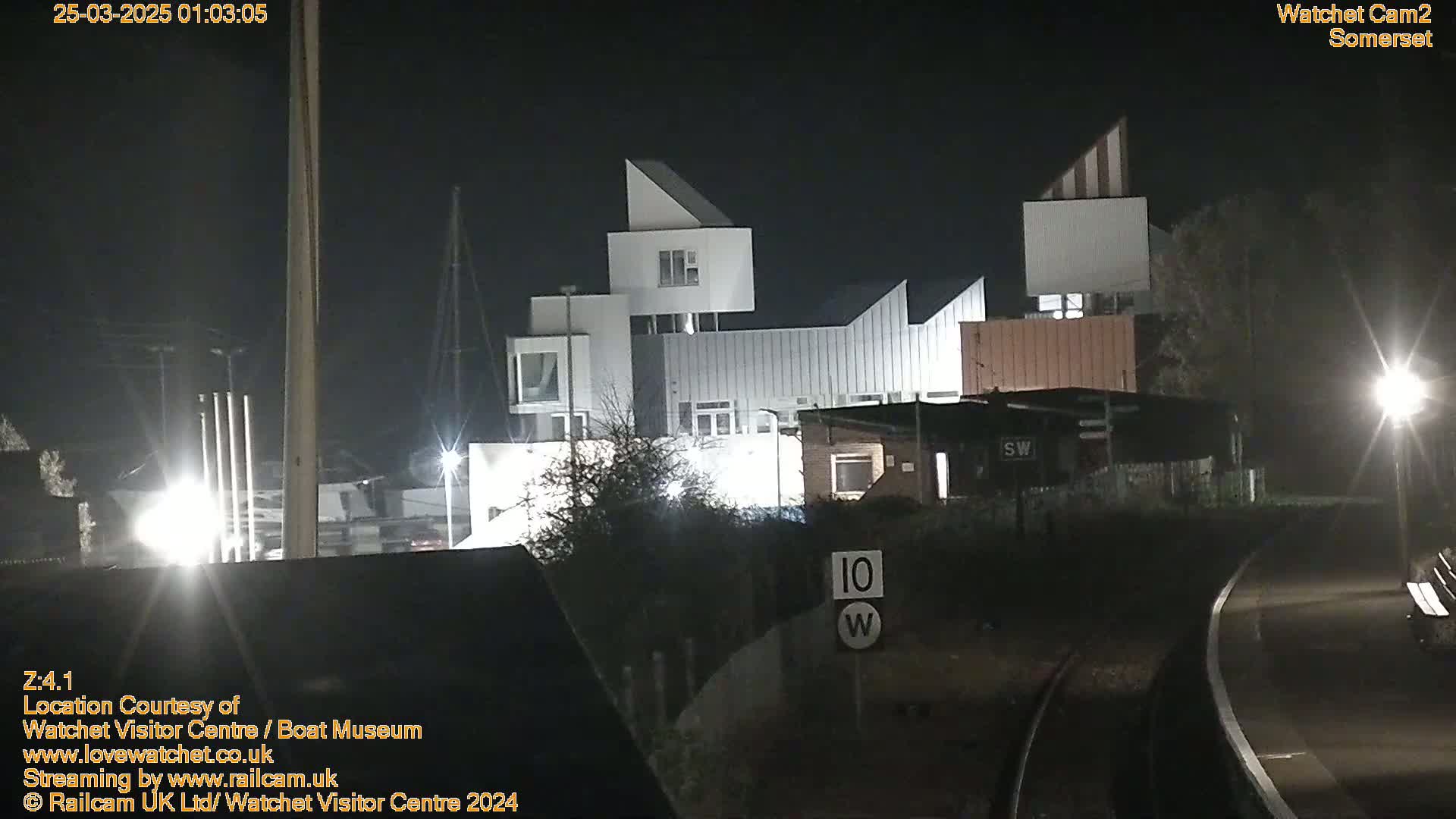 A modern, angular building complex is illuminated at night near railroad tracks.